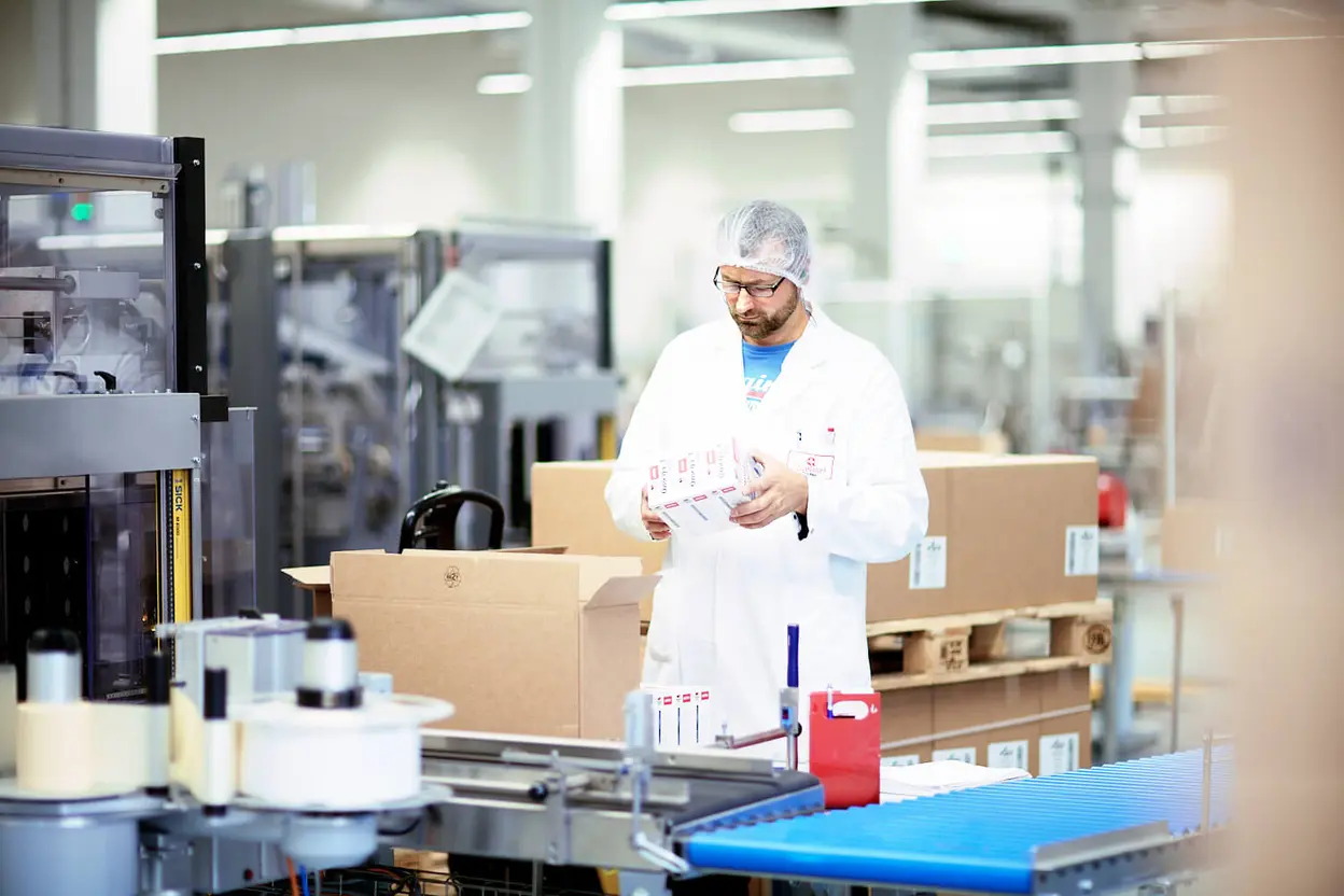 Mitarbeiter in der Produktion von Queisser Pharma hält Doppelherz-Produkte in der Hand