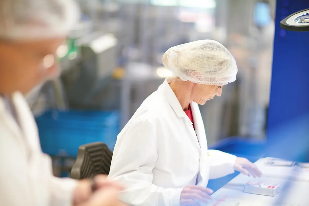 Mitarbeiterin in weißem Laborkittel und Haarnetz arbeitet mit Doppelherz-Verpackungen.
